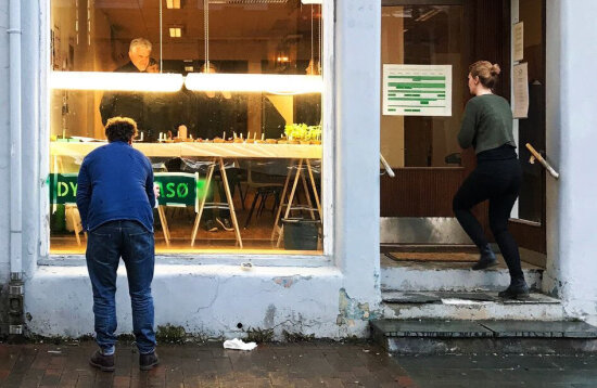 En dame går inn på Levende lokalers arrangement i Tromsø. En mann kledd i blått står utenfor og ser inn på det som skjer.