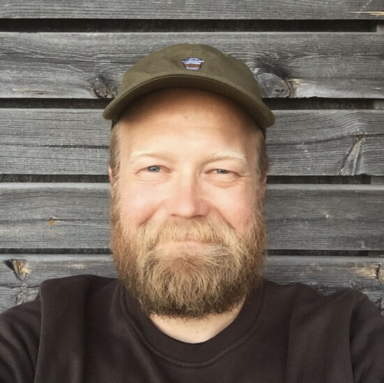 Selfie-portrett av en mann med stort, lyst skjegg og olivengrønn caps.