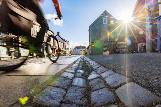 Silhuett av en lastesykkel som kjører oppover en brolagt gate. Solen titter over hustakene på Bakklandet i Trondheim.