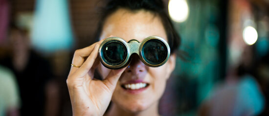 En dame ser i en kikkert – sett rett forfra.