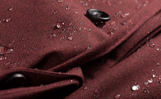 Nærbilde av et ytterplagg i burgunder, med regndråper.