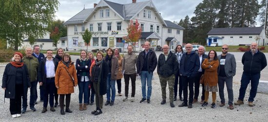 Mennesker på rekke og rad foran et eldre, hvitt trehus.