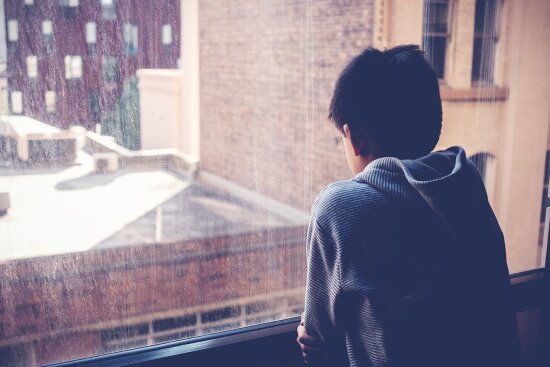 Preteen boy feeling lonely, looking out of window from his room, social distancing, isolation, mental health concept