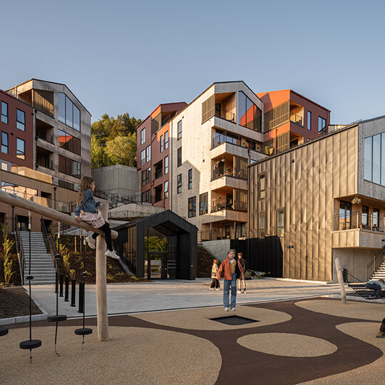 Barn som leker på en lekeplass foran et boligområde.