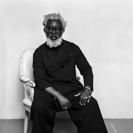 Portrett av en sortkledd T-Michael sittende i en stol.