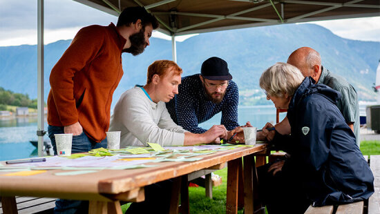 Innbyggerverksted i Aurland kommune: Mennesker sitter under et partytelt på kaia i Aurland.