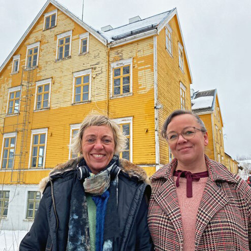 En mann og en kvinne foran et stort, gammelt gult trehus.
