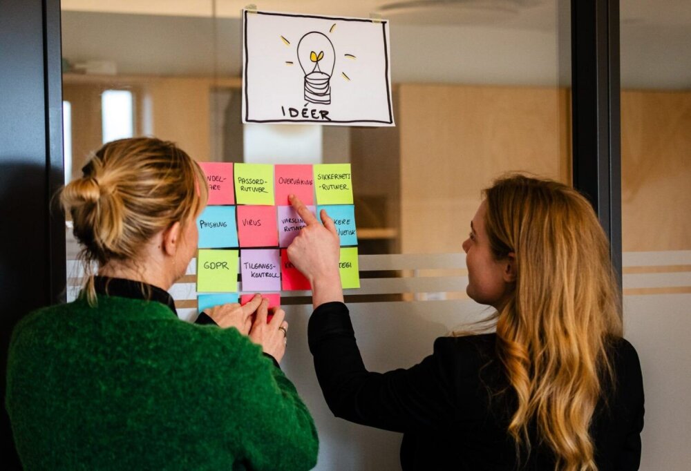 To personer peker på post-it lapper på veggen