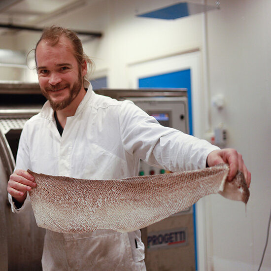 Bildet viser en mann i laboratoriefrakk som holder opp et bearbeidet fiskeskinn.
