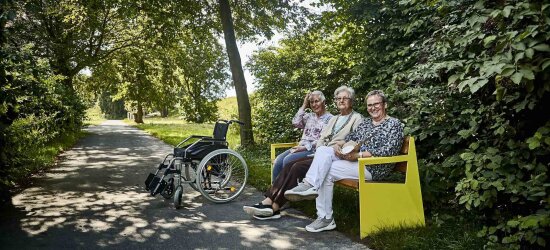 Bildet viser tre kvinner som sitter på en benk, en rullestol står ved siden av.