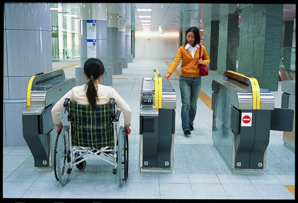 woman in wheelchair entering the station through the gate