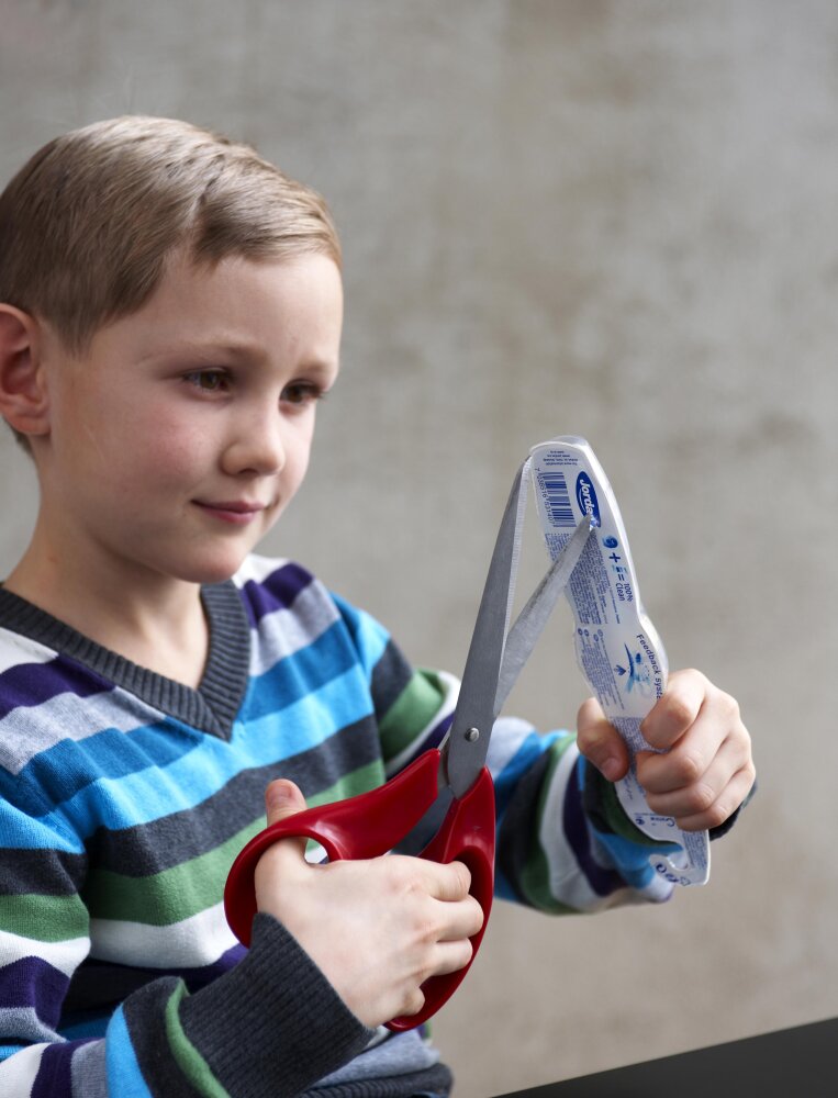 Child trying to open toothbrush packaging with scissors