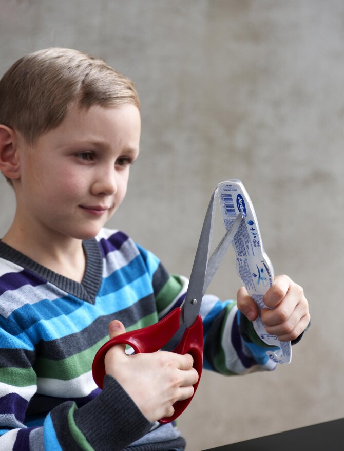 Child trying to open a toothbrush package with scissors