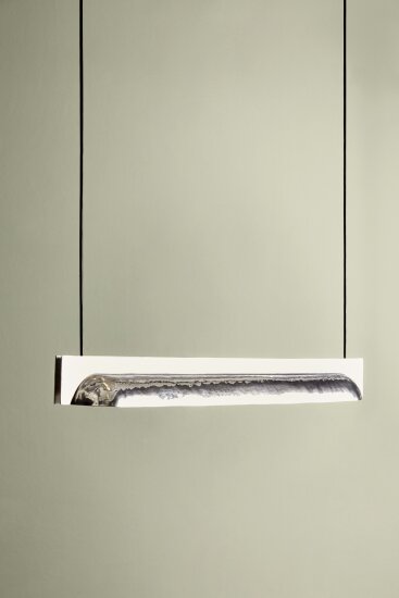 En smal rektangulær lampe som henger i to lange ledninger festet i hver sin ende av rektangelet. Lampen er laget av aluminium og er design av Stine Aas. Den skal stilles ut ved den norske fellesutstillingen under Milano Design Week 2019.