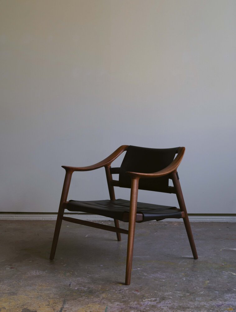 En lenestol i mid-century modern-stil i rødbrunt tre og sort skinn.
