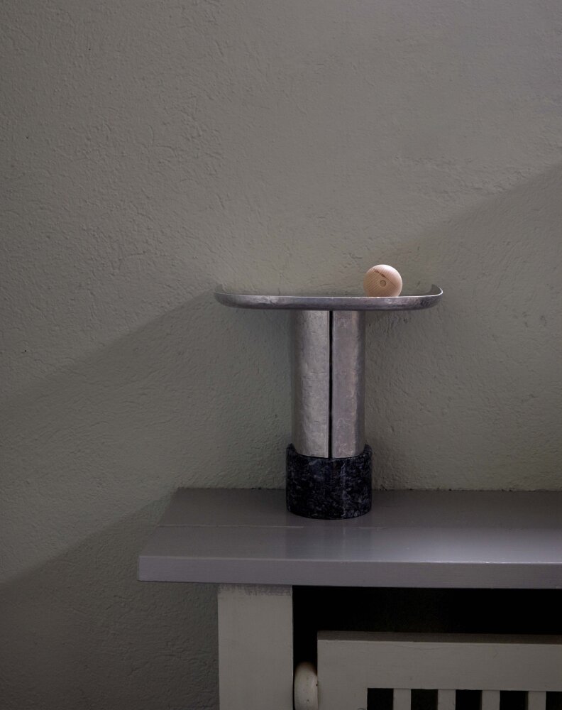 En liten hylle i rå, ubehandnlet aluminium mot enn grå murvegg.