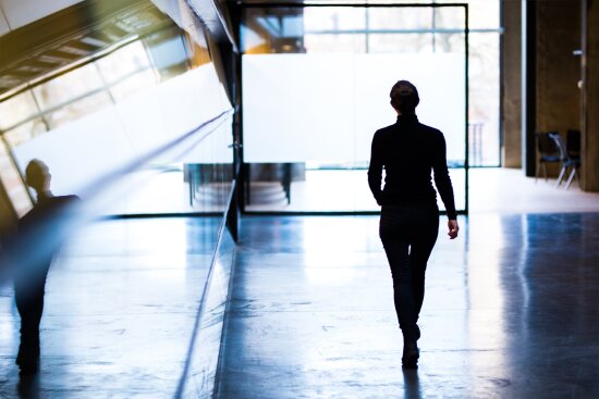 Kvinne går mot lys inne på DOGA-huset i Oslo. Hun er kledd i sort, har håret i knute og man kan kun se ryggen hennes.