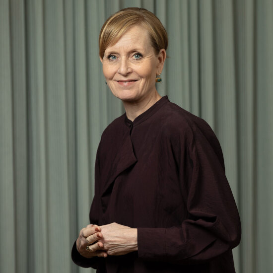 En smilende Benedicte med oppsatt blondt hår, burgunderrød bluse og øredobber med grønn stein.