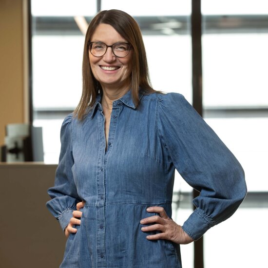 Ellen har på seg briller og en kjole i denim, og smiler mot kamera.