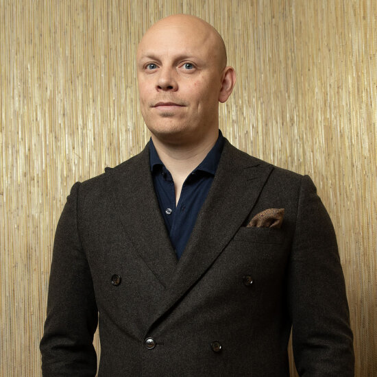 Jørgen med et direkte, vennlig blikk og glattbarbert hode. Han har på seg blå skjorte og brun blazer med et tørkle stikkende opp fra brystlommen.