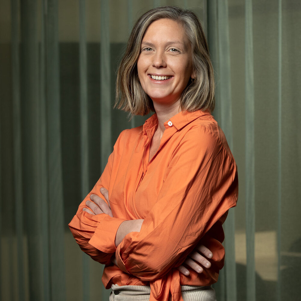 En smilende Siri med halvlangt blondt hår og oransje bluse. 