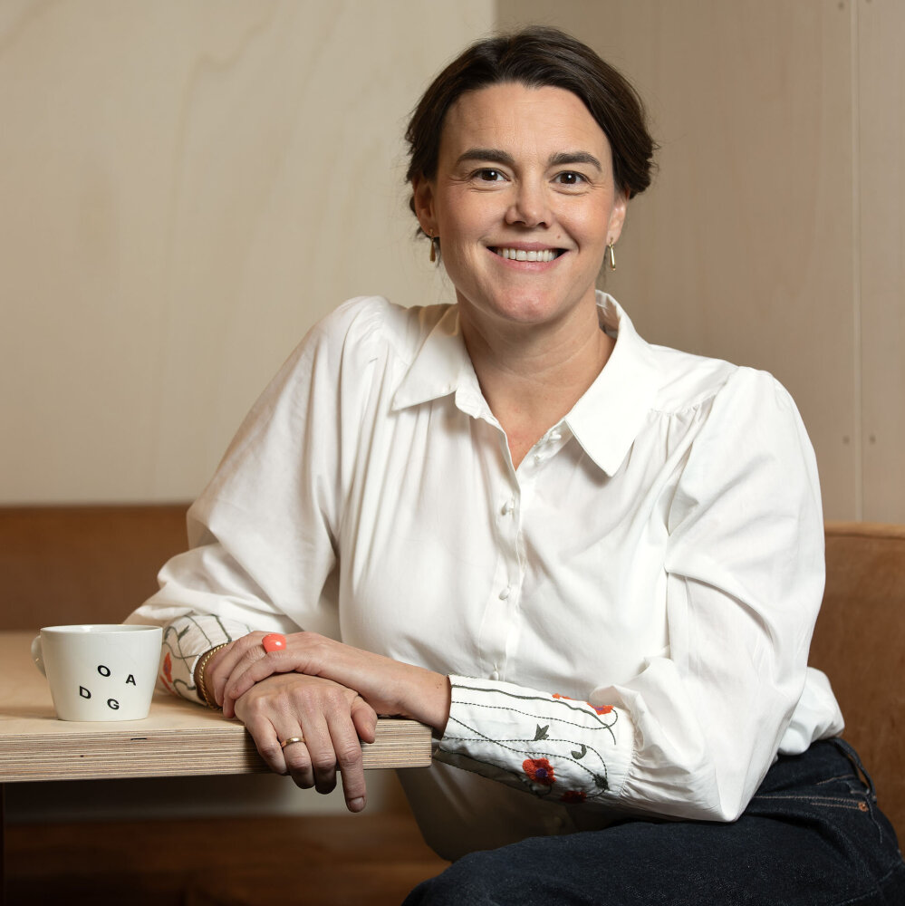 Sissel smiler med mørkt oppsatt hår og hvit bluse med broderier på mansjettene. 