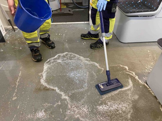 Interiør med trikkegulv med beina til to rengjøringspersonell med bøtte og vann. Foto