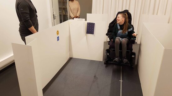 Jente i elektrisk rullestol trillet inn i en pappmodell av Trikken. Foto