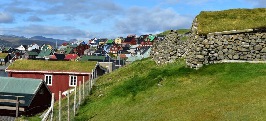 Fargerike trehus hus  mot grønne gressbakker med murer av naturstein.  Blå  himmel med gråblå skyer.