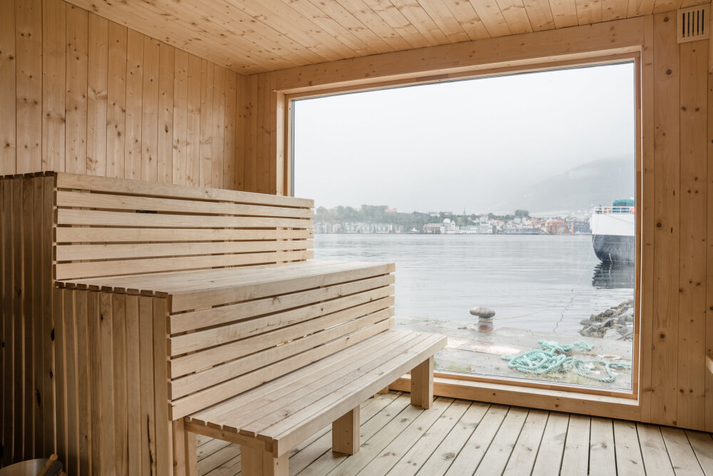 Badsturom med benker og et stor vindu med utsikt mot sjøen, med en båt ankret opp utenfor. 