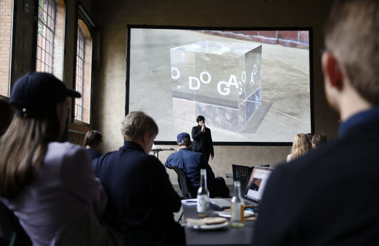 Juryering av DOGA-merket for design og arkitektur i Hallen på DOGA. Juryleder Torun Degnes står på en scene og snakker til juryen. På en skjerm vises plaketten for DOGA-merket: en glasskube med bokstavene D, O, G, A i hvitt.