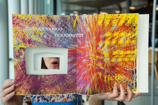 Hender som holder en bok åpen med spraglende mønster i flere farger.