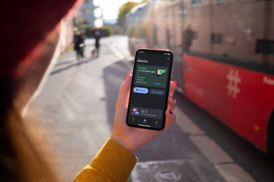 Hånd holder en smarttelefon som viser en forsiden av den nye Ruter appen. Foto