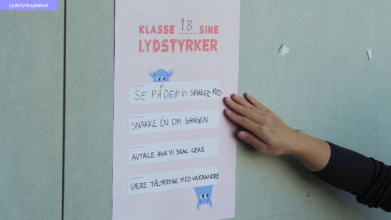 Hvit plakat med 1Bs lydstyrker skrevet på. Foto