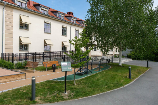 Bygård med anlagt park foran, med trær, benker og aktiviteter.