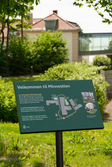 Grønt informasjonsskilt som står ute i en hage. Foto