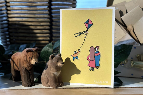 Illustrert kort med to damer som ser på en gutt som flyr drage.