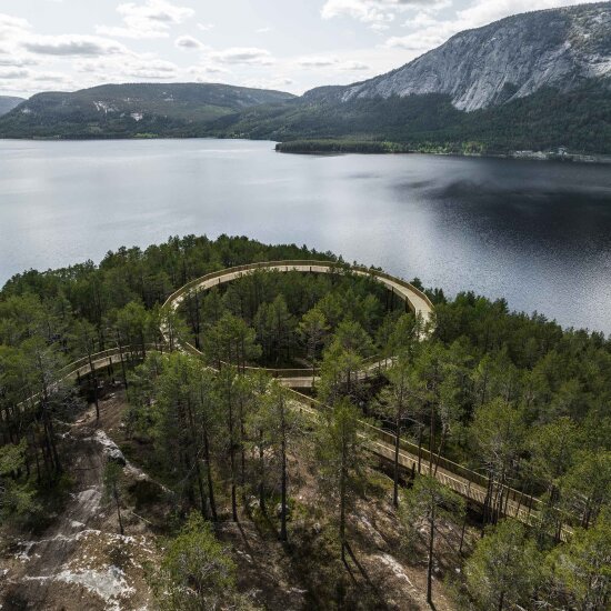 Skog og vann, med gangvei synlig gjennom skogen. Dronefoto