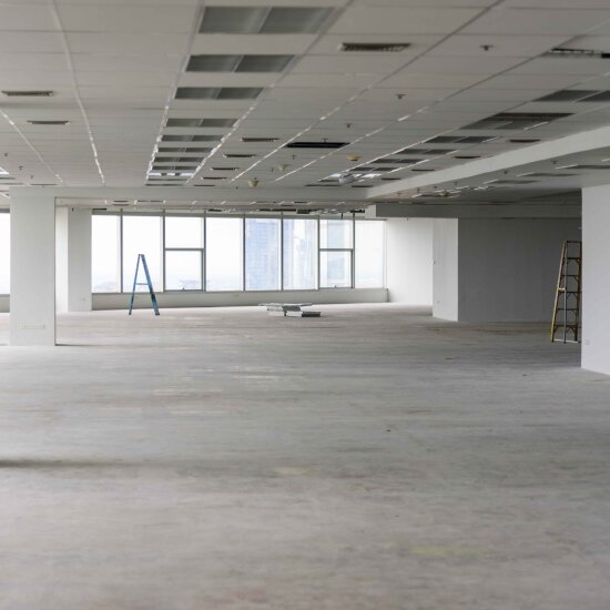 Et tomt og nakent kontorlokale med store vinduer. To trappestiger står tilfeldig plassert.