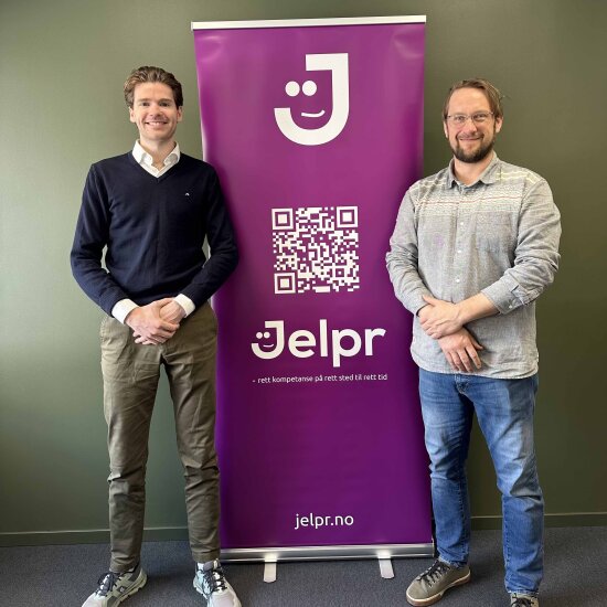 To menn på hver sin side av en lilla roll-up, med en stor qr-kode og teksten Jelpr, rett kompetanse til rett tid.