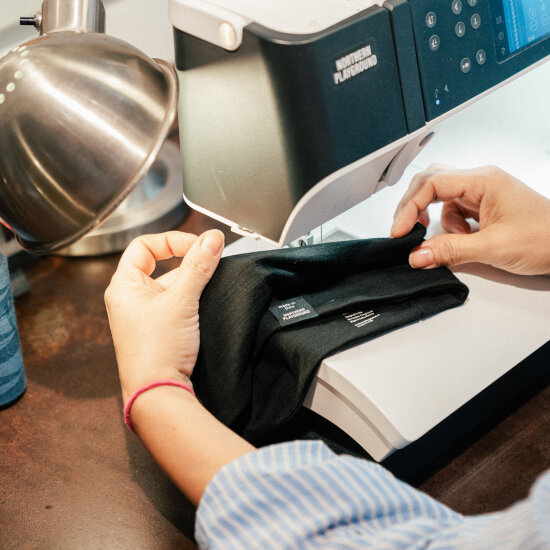 To hender holder et sort stoffstykke inn mot en symaskin.