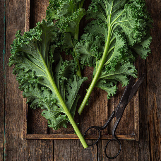 Grønnkålblader og en rusten saks på et brett i mørkebrunt treverk.