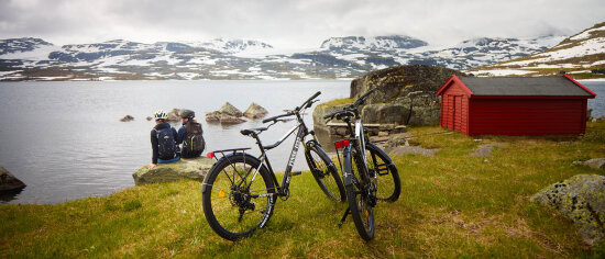 To parkerte sykler og to jenter med sykkelhjelm som sitter på en stein og ser utover et fjellandskap