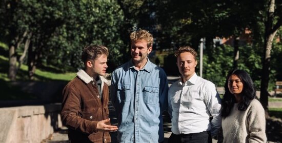 Tre menn og en kvinne oppstilt for fotografering mot en bakgrunn av grønne trær.