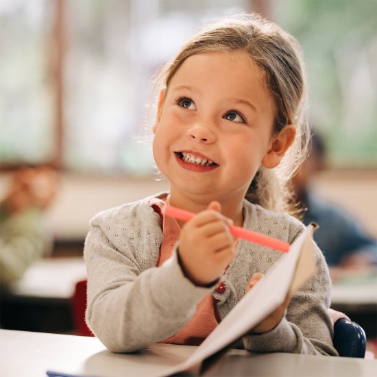 En liten skolejente smiler og peker med en oransje tusj i en bok.