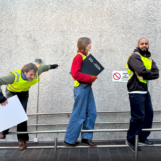 Tre ungdommer med grønn synlighetsvest balanserer på et rekkverk.