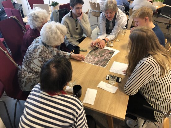 Workshop. Unge og eldre mennesker rundt et bord. Møteleder peker på et bilde. Testing av senior- og ungdomstråkk i Drammen med Guri Mette Vestby, NIBR Oslo Met