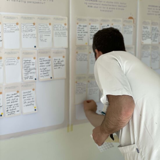 En mann i sykehusklær setter opp en lapp på en tavle.