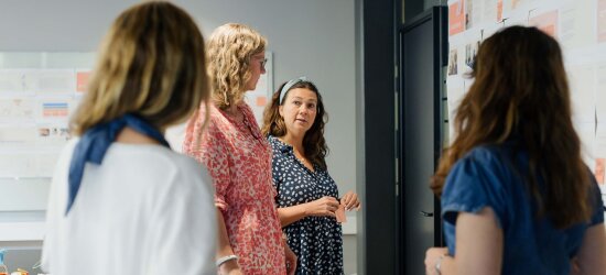 Fire kvinner står foran en tavle og snakker sammen.