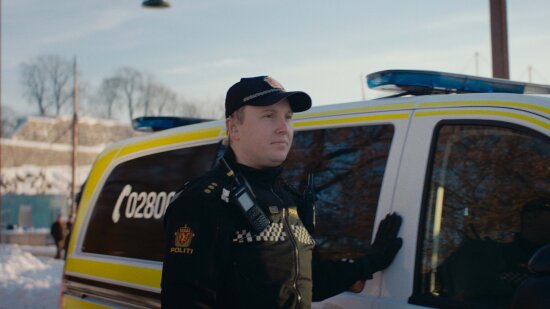 Politimann foran en politibil. Foto.